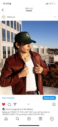 a man in a brown jacket and hat is posing in front of a building